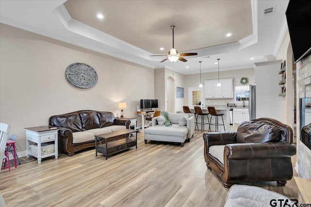 living room featuring ornamental molding, a raised ceiling, ceiling fan, and light wood-type flooring