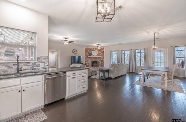 kitchen with sink, white cabinetry, a brick fireplace, hanging light fixtures, and stainless steel dishwasher