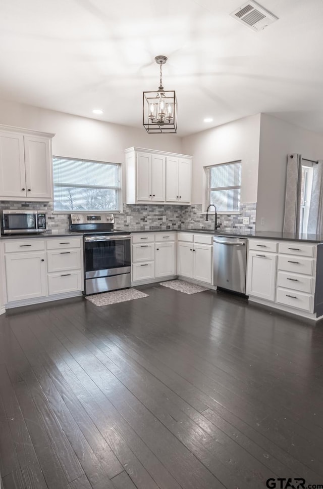 kitchen with white cabinetry, appliances with stainless steel finishes, dark hardwood / wood-style floors, and hanging light fixtures