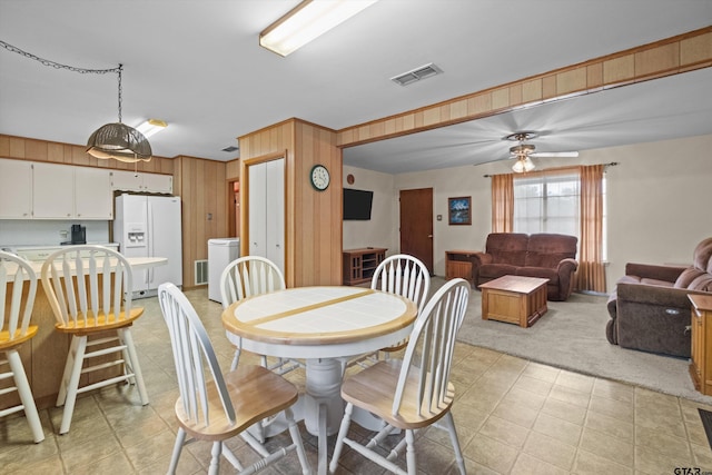 carpeted dining space with wood walls and ceiling fan