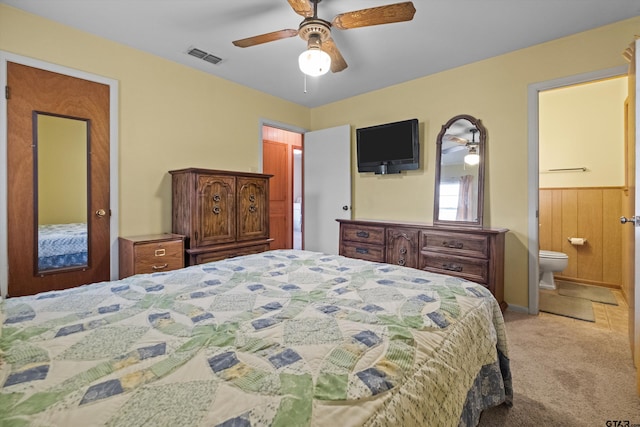 carpeted bedroom featuring ensuite bathroom, ceiling fan, and wooden walls