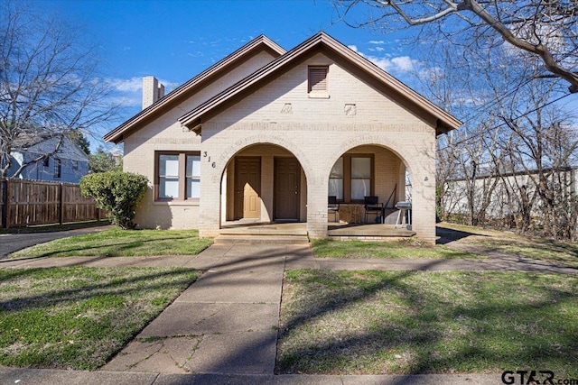 view of front of property featuring covered porch, brick siding, fence, a chimney, and a front yard