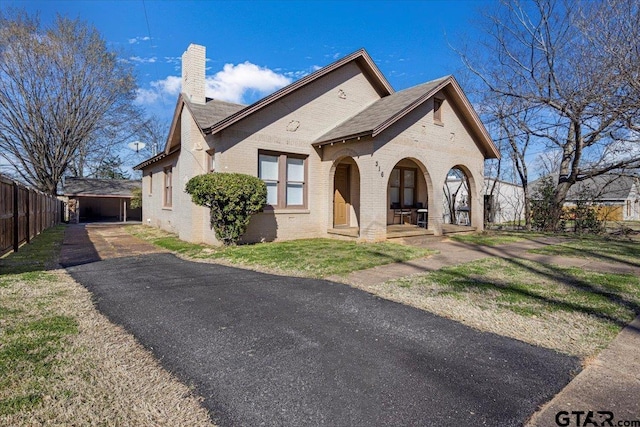 view of front of house with brick siding, a chimney, a porch, and fence