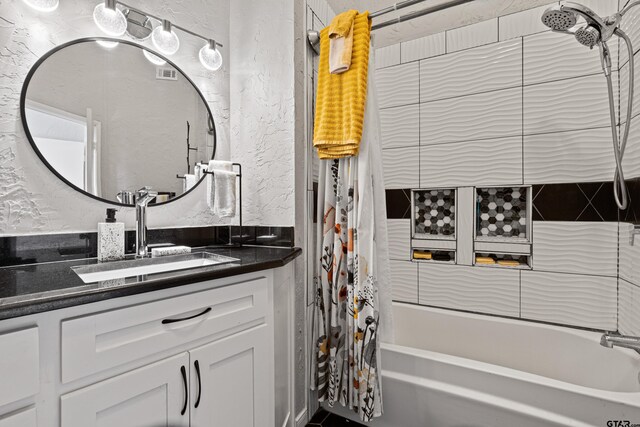 full bathroom featuring vanity, a textured wall, shower / bath combination with curtain, and visible vents