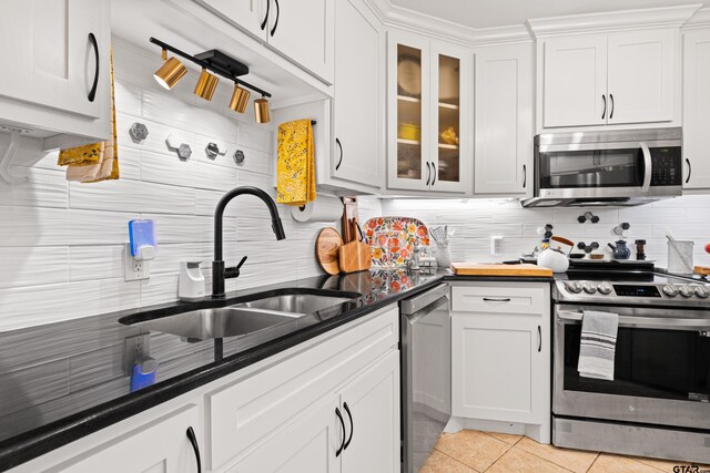 kitchen featuring white cabinetry, light tile patterned floors, a sink, appliances with stainless steel finishes, and backsplash
