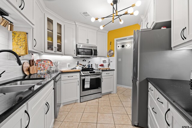 kitchen with an inviting chandelier, decorative backsplash, white cabinetry, a sink, and appliances with stainless steel finishes