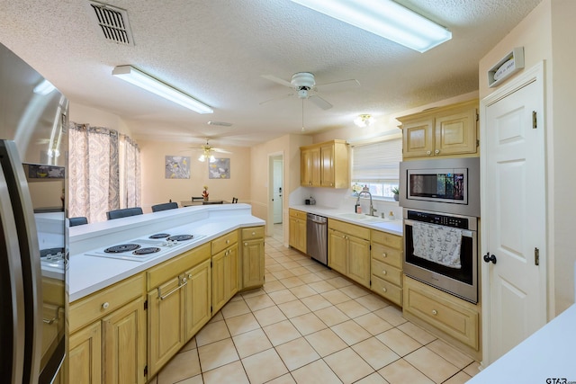 kitchen with stainless steel appliances, sink, light brown cabinetry, a textured ceiling, and light tile patterned floors