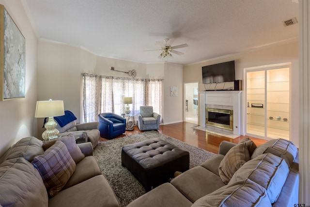 living room featuring a textured ceiling, hardwood / wood-style flooring, ceiling fan, crown molding, and a fireplace