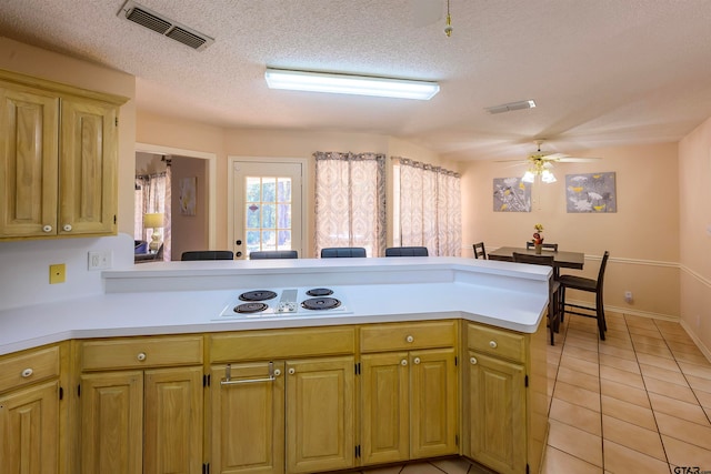 kitchen with a textured ceiling, kitchen peninsula, ceiling fan, and light tile patterned floors