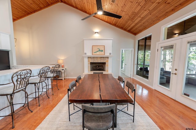 dining space featuring light wood-style flooring, a tile fireplace, wood ceiling, and ceiling fan