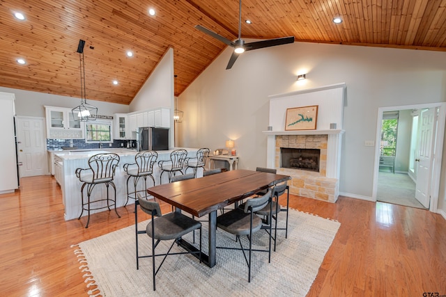 dining area featuring wooden ceiling, a stone fireplace, high vaulted ceiling, and ceiling fan