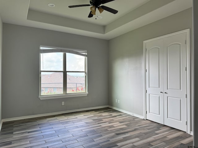 empty room featuring light wood-type flooring, ceiling fan, and a raised ceiling