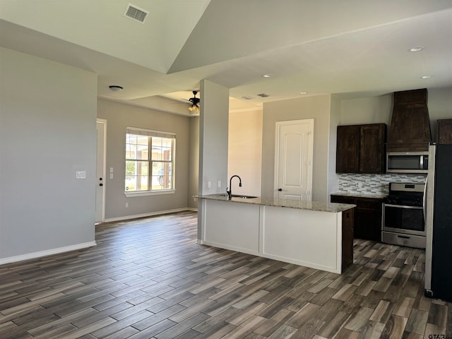 kitchen featuring dark brown cabinetry, appliances with stainless steel finishes, light stone countertops, ceiling fan, and dark hardwood / wood-style floors