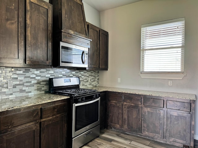 kitchen featuring dark brown cabinetry, light stone countertops, light hardwood / wood-style flooring, and appliances with stainless steel finishes