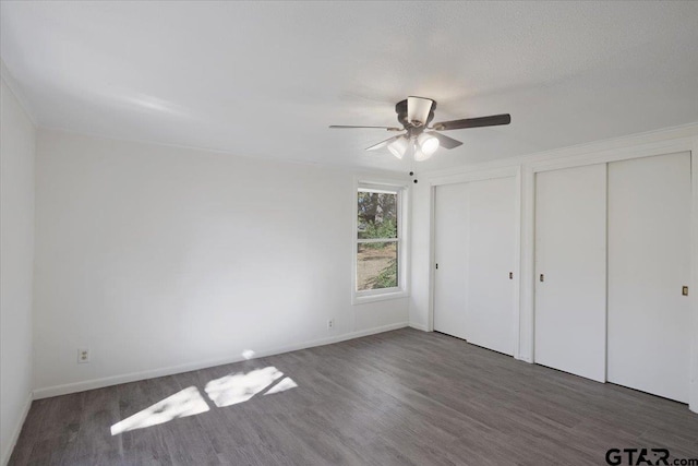 unfurnished bedroom featuring dark wood-type flooring, ceiling fan, and multiple closets