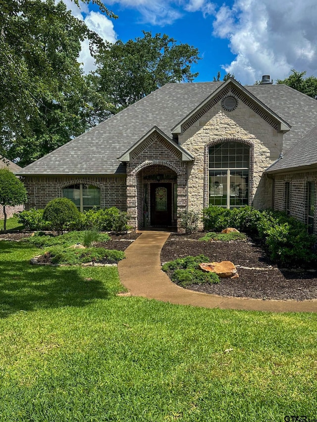 french country inspired facade with a front yard, brick siding, and roof with shingles