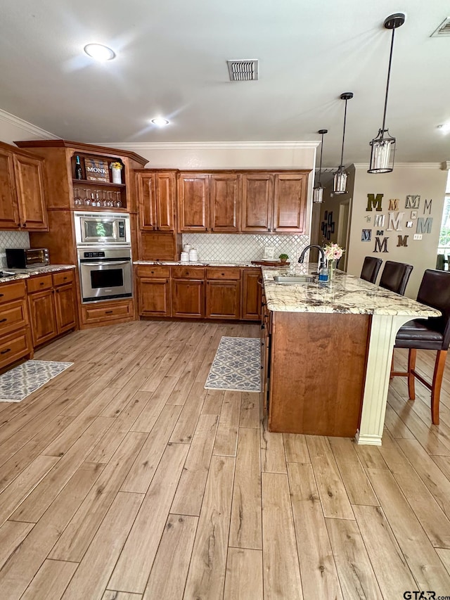 kitchen with stainless steel appliances, a sink, a kitchen bar, brown cabinetry, and decorative backsplash