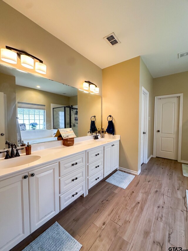 full bathroom with a shower stall, wood finished floors, double vanity, a bath, and baseboards