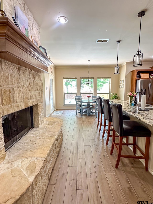 living area featuring light wood-type flooring, ornamental molding, a stone fireplace, and baseboards