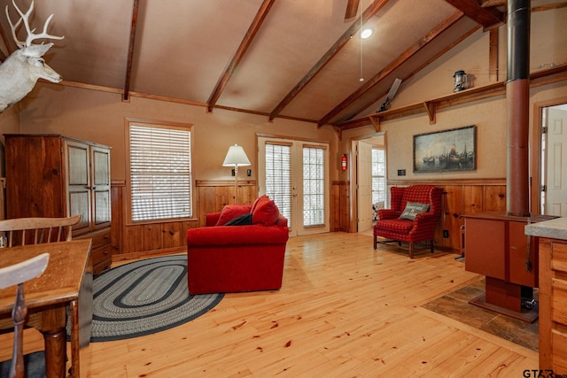 living room featuring a wood stove, light wood-type flooring, a wealth of natural light, and vaulted ceiling with beams