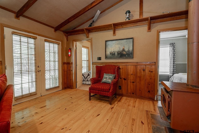 living area featuring a wealth of natural light, light hardwood / wood-style floors, lofted ceiling with beams, and wooden walls