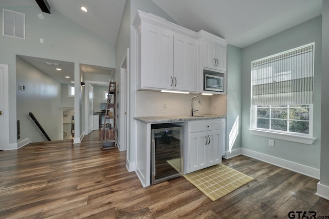 kitchen featuring wine cooler, stainless steel microwave, tasteful backsplash, and white cabinets