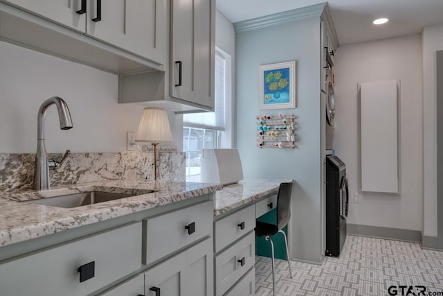 kitchen featuring stacked washer / dryer, crown molding, sink, and light stone counters