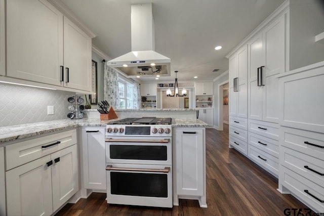 kitchen featuring double oven range, kitchen peninsula, pendant lighting, island exhaust hood, and white cabinets