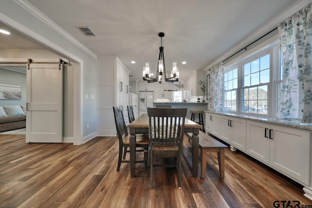 dining room with crown molding, a barn door, dark wood-type flooring, and a notable chandelier