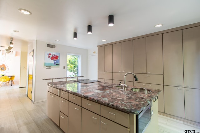 kitchen featuring sink, dark stone counters, an island with sink, gray cabinets, and black electric stovetop