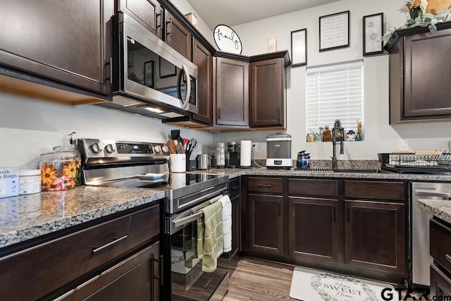 kitchen featuring light wood finished floors, stone countertops, stainless steel appliances, dark brown cabinets, and a sink