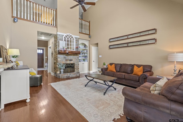 living room with a high ceiling, dark hardwood / wood-style flooring, a stone fireplace, and ceiling fan