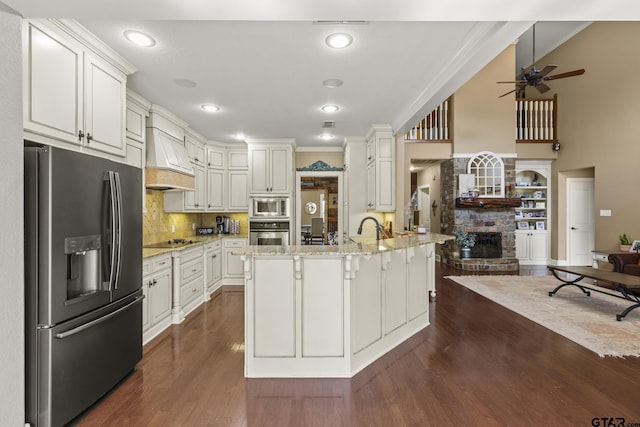 kitchen with light stone countertops, stainless steel appliances, a kitchen island with sink, and ornamental molding