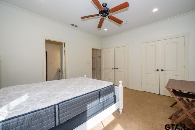 bedroom featuring ornamental molding, two closets, light colored carpet, and ceiling fan