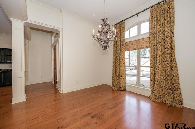 unfurnished dining area featuring a healthy amount of sunlight, ornamental molding, wood-type flooring, and ornate columns