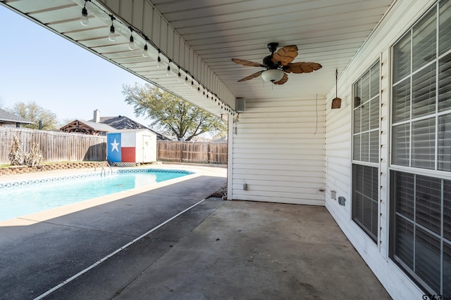 view of pool with an outbuilding, a ceiling fan, a patio, a fenced backyard, and a storage shed