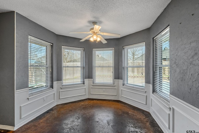 interior space featuring concrete floors, ceiling fan, wainscoting, a textured wall, and a textured ceiling