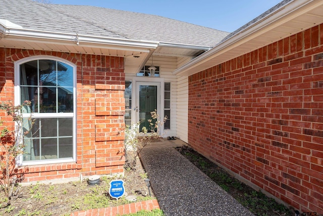 doorway to property with brick siding and roof with shingles