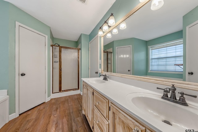 full bath featuring double vanity, a stall shower, wood finished floors, and a sink