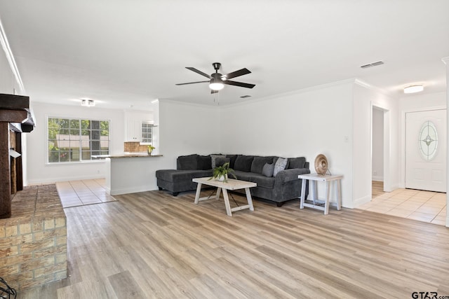living room featuring baseboards, ornamental molding, light wood-style floors, visible vents, and ceiling fan