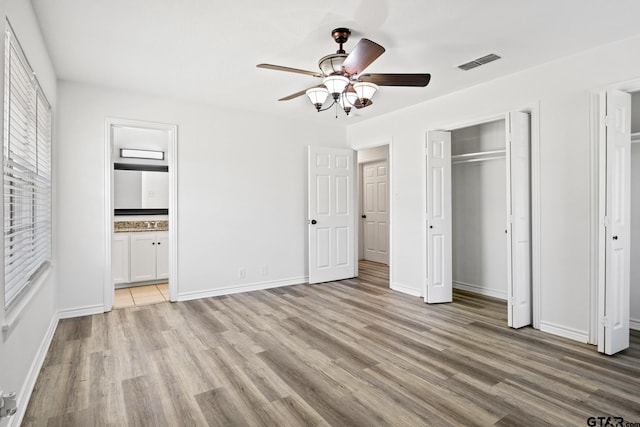 unfurnished bedroom with baseboards, ensuite bathroom, a ceiling fan, visible vents, and light wood finished floors