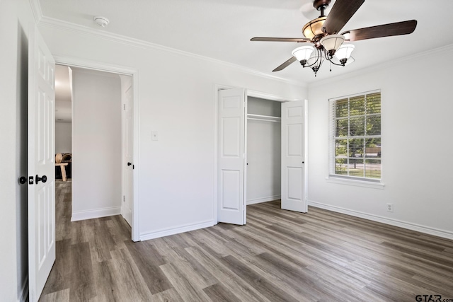 unfurnished bedroom with crown molding, ceiling fan, a closet, wood finished floors, and baseboards