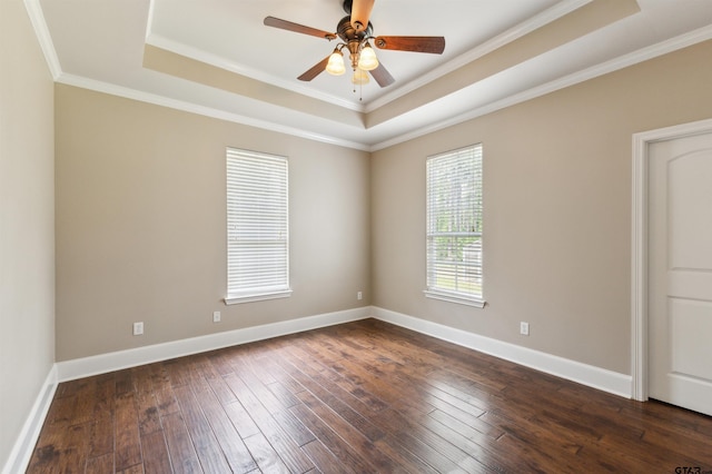 empty room featuring a raised ceiling, dark wood-style floors, ornamental molding, baseboards, and a ceiling fan