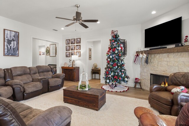 living room with light wood-type flooring, a stone fireplace, and ceiling fan