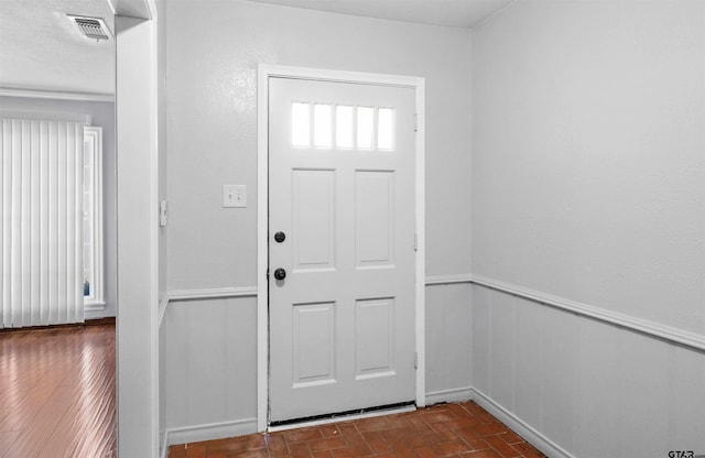 foyer with brick floor, visible vents, and wainscoting