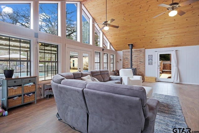 living room featuring french doors, wood ceiling, light hardwood / wood-style flooring, a wood stove, and ceiling fan