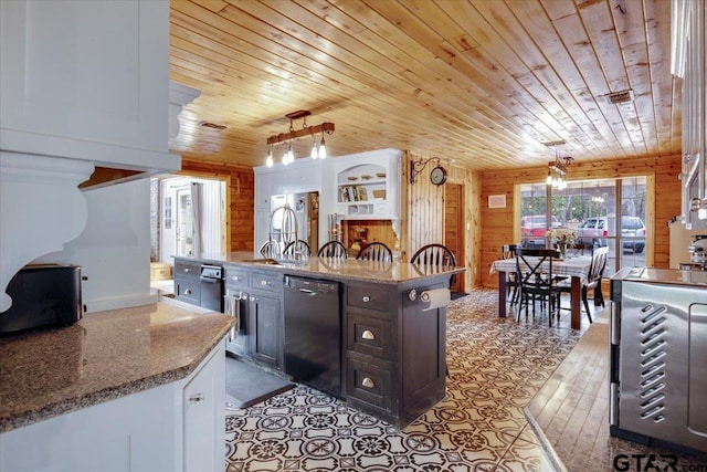 kitchen with hanging light fixtures, black dishwasher, dark brown cabinetry, light stone countertops, and wood walls