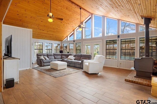 living room featuring wood ceiling, light hardwood / wood-style flooring, ceiling fan, high vaulted ceiling, and a wood stove