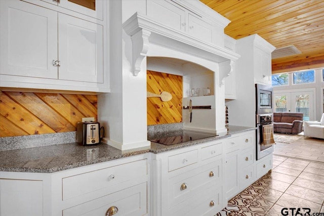 kitchen featuring white cabinetry, dark stone counters, light tile patterned floors, stainless steel appliances, and wooden ceiling