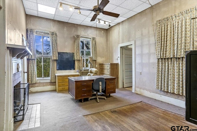 carpeted office space featuring a tiled fireplace, a towering ceiling, a drop ceiling, and ceiling fan